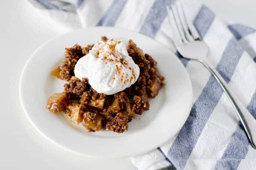 paleo apple crisp on a white plate topped with coconut whipped cream