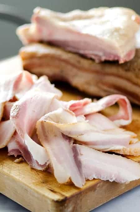 uncooked homemade bacon sliced on a cutting board