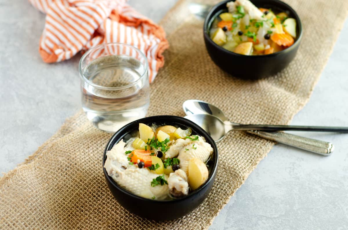 Two bowls of chicken. souse on a table with 2 spoons and a glass of water