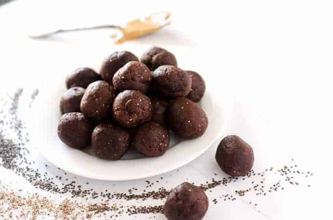 Side view of plate of energy balls surrounded by chia seeds, flax meal, and spoon with nut butter