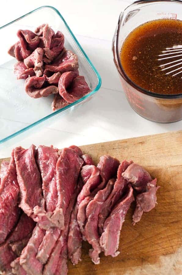 overhead view of raw meat on cutting board and in a pan with marinade next to it