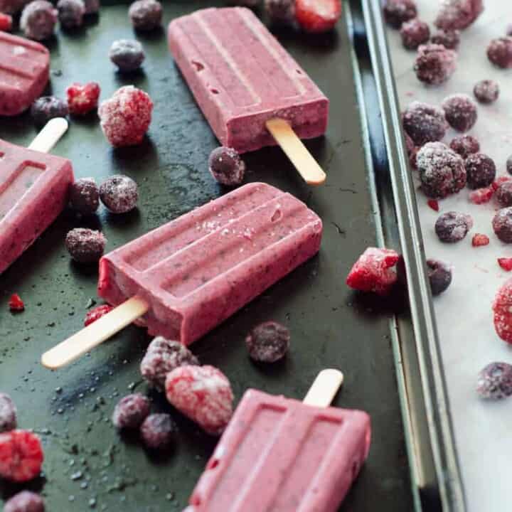 side view of berry popsicles on a baking sheet surrounded by frozen berries