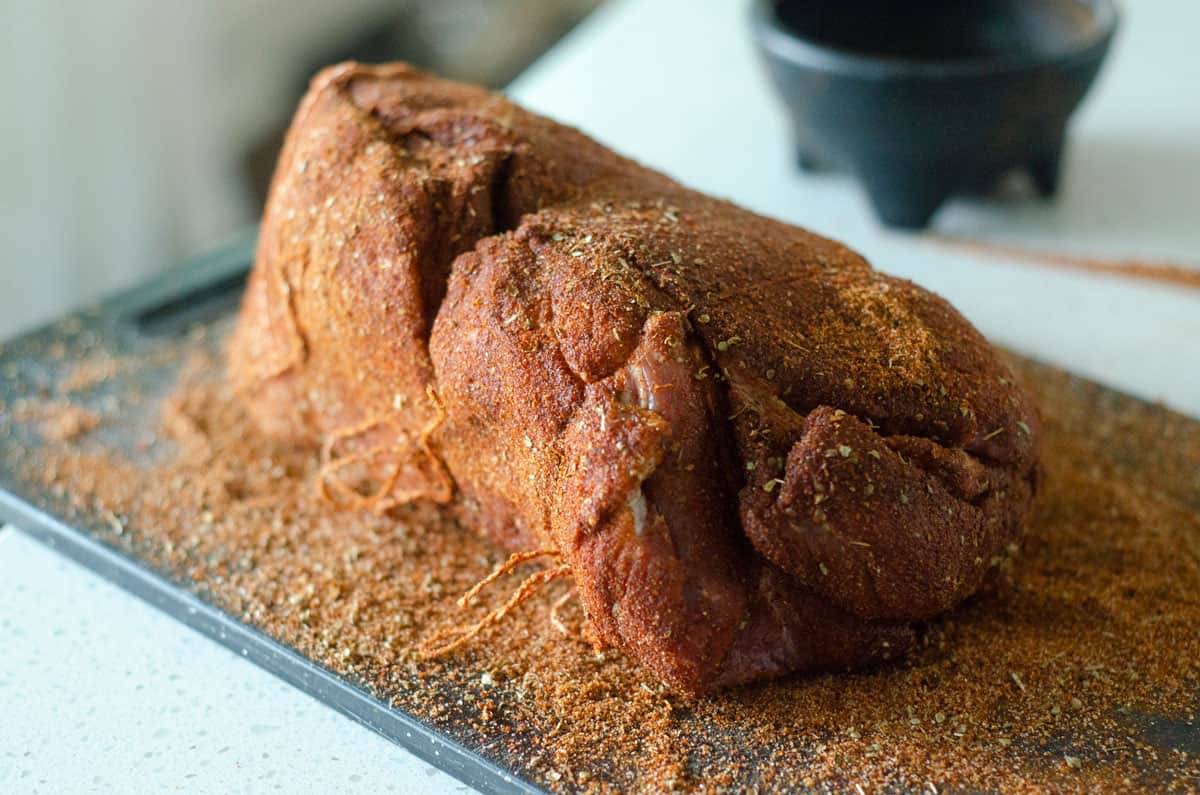 Pork butt on cutting board fully coated in dry rub