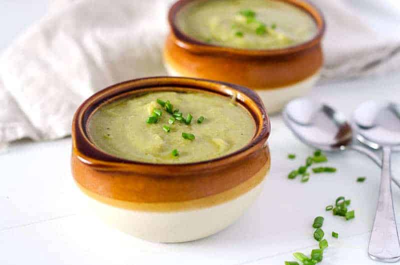 Two brown crocks of dairy free broccoli soup on table with two spoons next to them