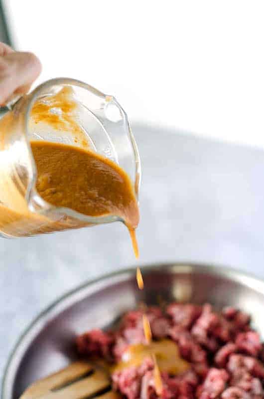 hand pouring bulgogi sauce into pan of cooking meat