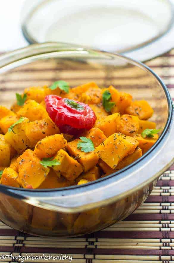 Glass bowl of caribbean pumpkin curry topped with parsley and a scotch bonnet pepper