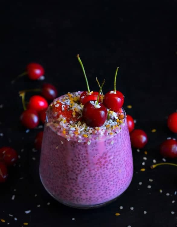 side view of berry chia pudding topped with cherries on a dark background