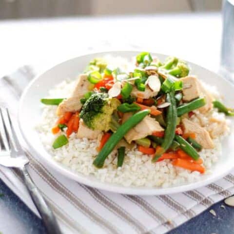 plate of paleo chicken stir fry on top of a striped napkin with a fork and glass of water