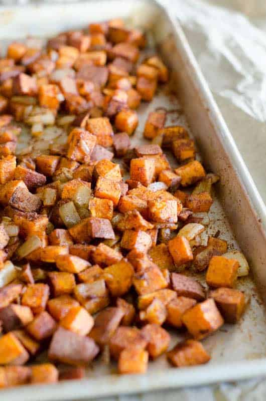 Side view of baking sheet full of cinnamon roasted sweet potatoes with onions