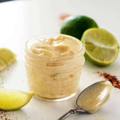 jar of chipotle lime mayo surrounded by chili powder limes and a spoon