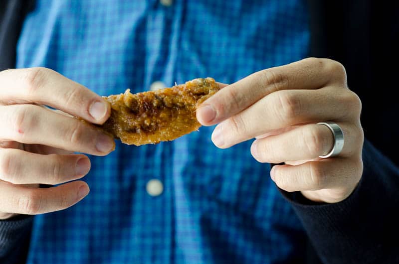 close up of a mans hands holding a chicken wing