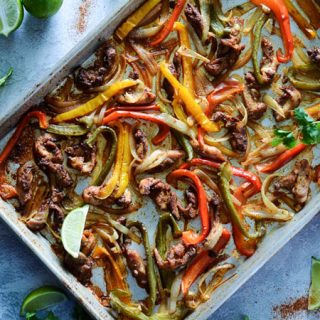 overhead view of baking sheet with peppers, onions and chicken baked on it surrounded by peppers cilantro and limes