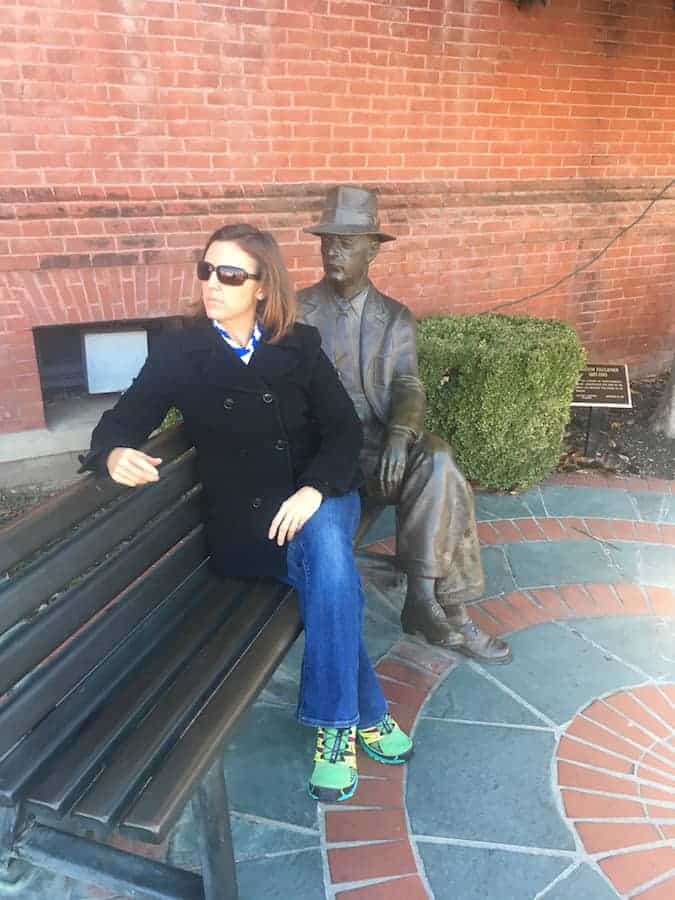 Woman sitting on bench with William Faulkner statue, mimicking his pose