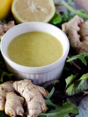 bowl of ginger dressing surrounded by lettuce, ginger, and lemons