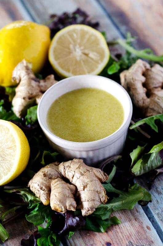 bowl of ginger dressing surrounded by lemons, ginger, and lettuce leaves