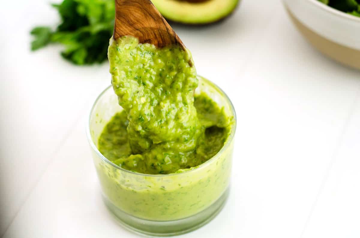 copycat Trader Joe's green goddess dressing in a glass bowl dripping off a wooden serving spoon