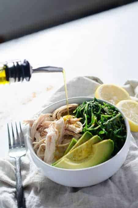 autoimmune healing bowl full of chicken, arugula and avocado being drizzled with olive oil