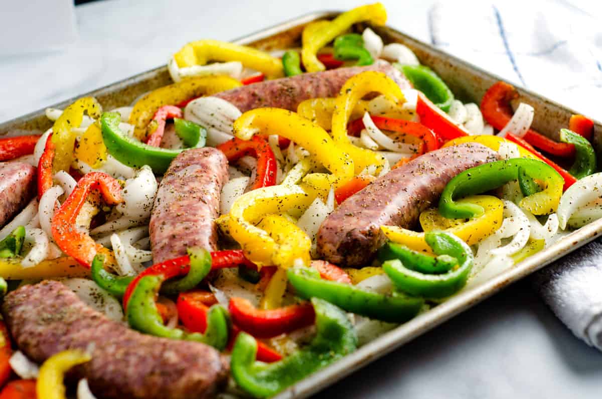 Metal sheet pan with raw sausage and peppers and onions on it