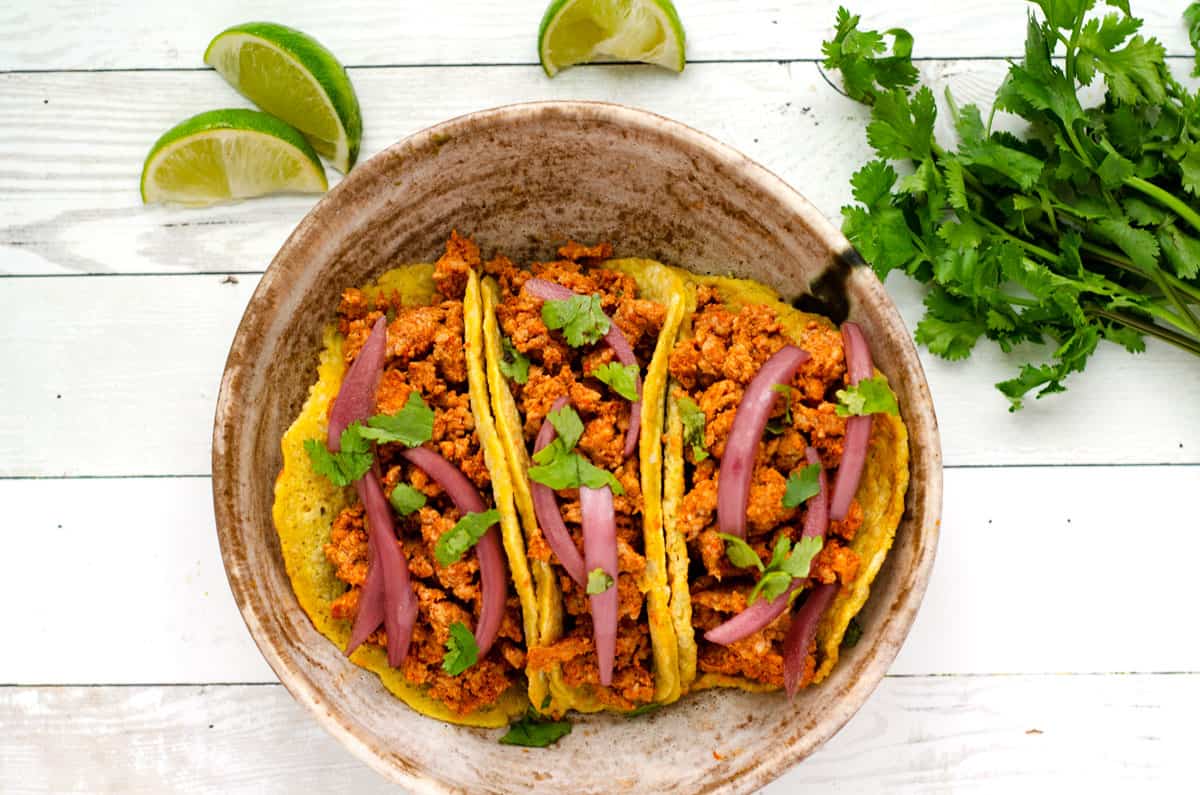 Overhead view of chorizo breakfast tacos in a bowl surrounded by lime slices and cilantro