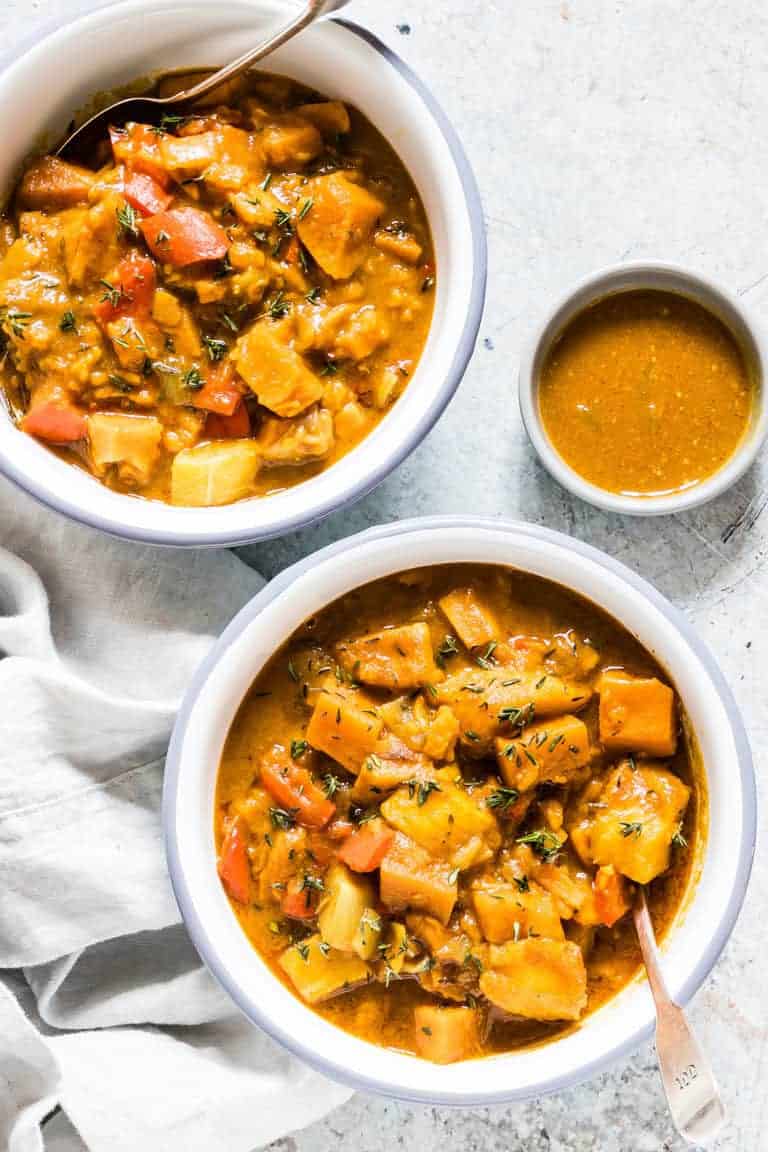 Two servings of Instant Pot Pumpkin and Plantain Curry served in white bowls with a small bowl of curry sauce and a white cloth napkin