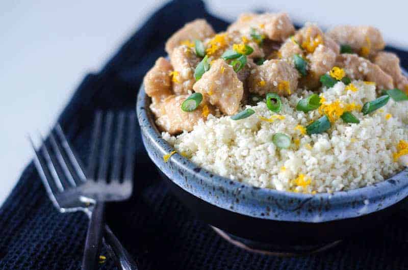 side view of a bowl of Instant Pot orange chicken and cauliflower rice topped with green onions and orange zest