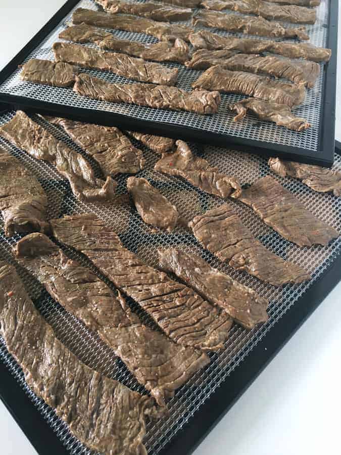 strips of marinated meat on dehydrator trays for paleo beef jerky