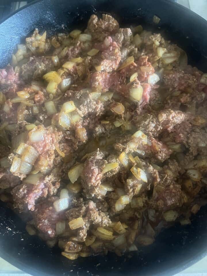 ground lamb, onions, and seasoning cooking in cast iron skillet