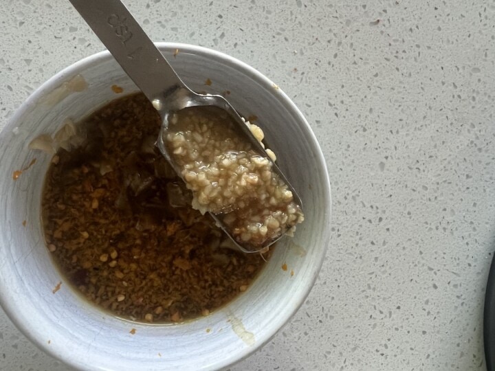 bowl of orange sauce with spoon of garlic being added