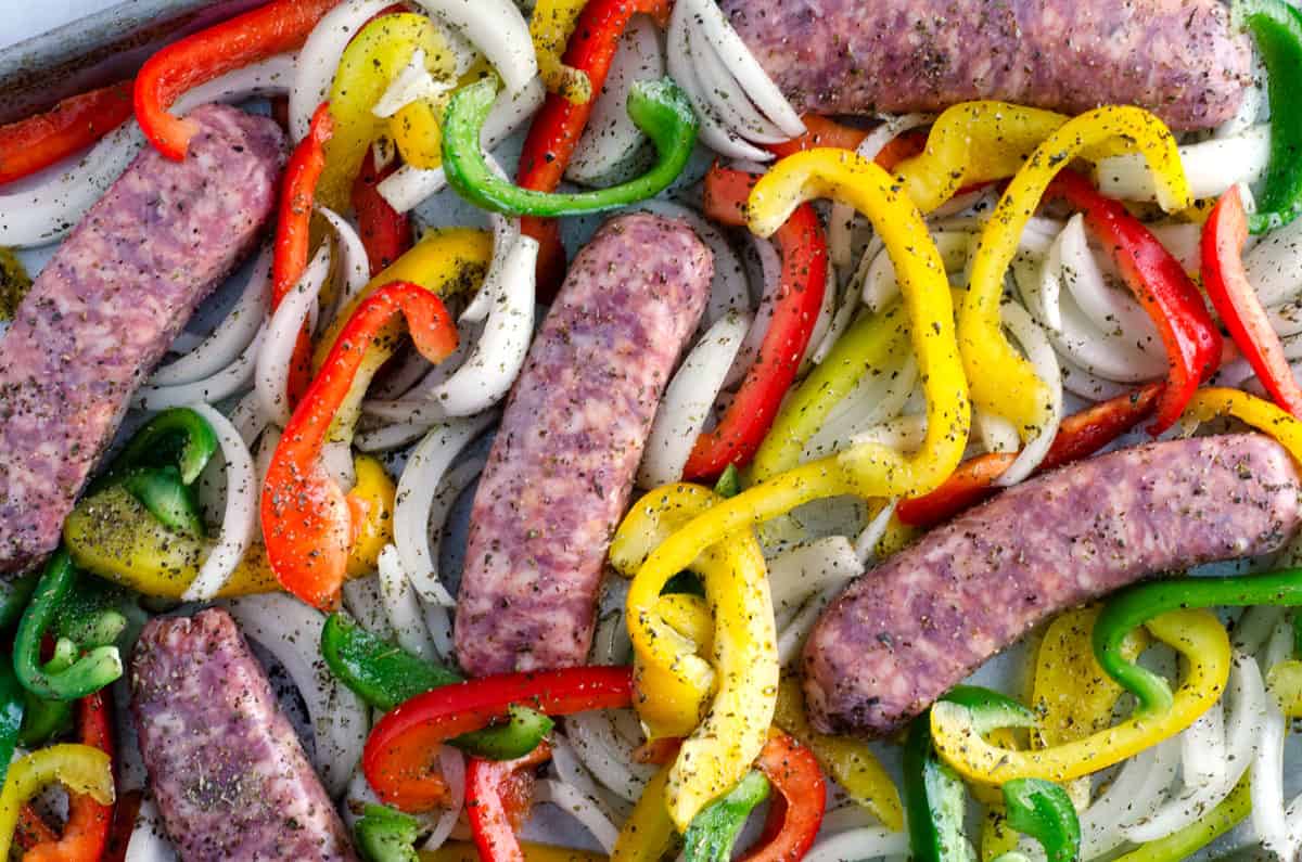 Overhead view of raw sausage, peppers, and onions with spices