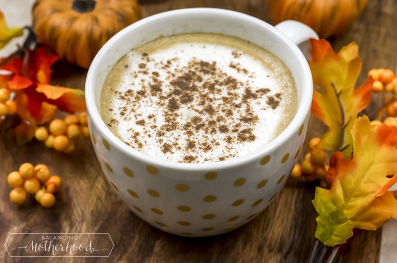 Mug of paleo pumpkin latte in a polka dot mug surrounded by fall colored leaves