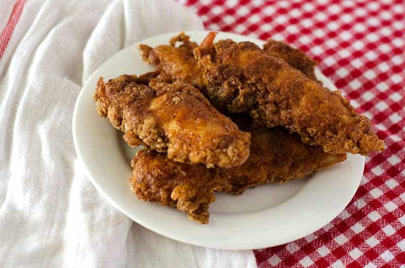 gluten free nashville hot chicken fingers on a plate with a white and red checkered tablecloth