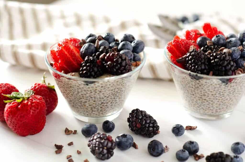 side view of two parfait cups filled with chia seed pudding with almond milk topped with fresh berries and cocoa nibs