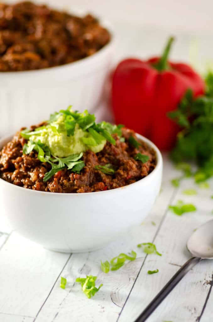 Close up side view of a white bowl full of paleo chili topped with avocado cream and fresh chopped herbs