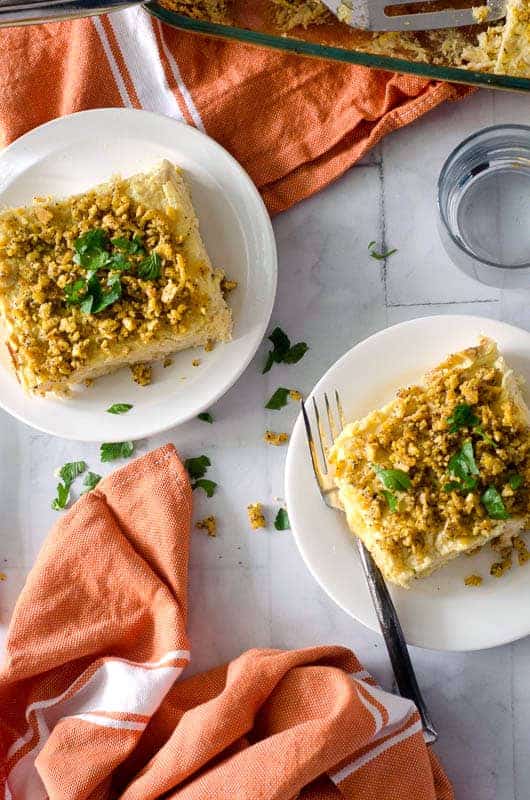 Overhead view of two plates with chicken casserole servings on them, topped with fresh parsley and a casserole dish and orange napkins in the background