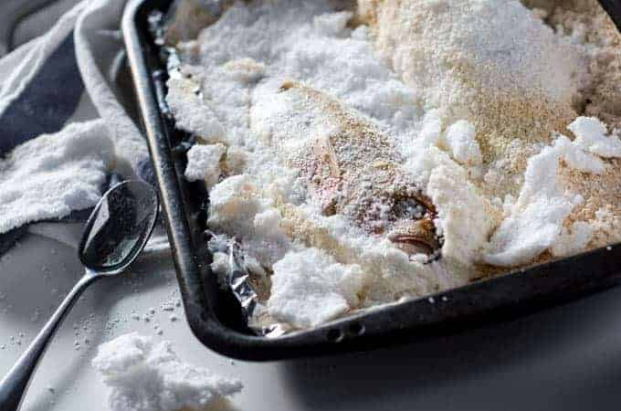 roasting pan lined with foil with a salt baked fish on it with the salt crust broken open and a spoon lying nearby