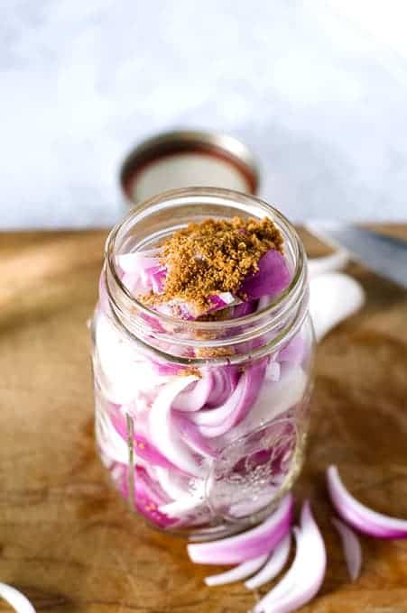 Overhead view of the top of a mason jar packed with red onion slices sprinkled with sugar and salt