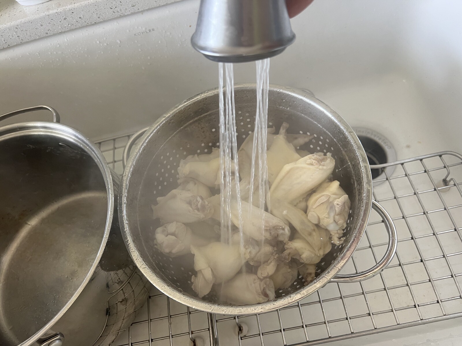 Colander in sink with faucet rinsing chicken wings in sink