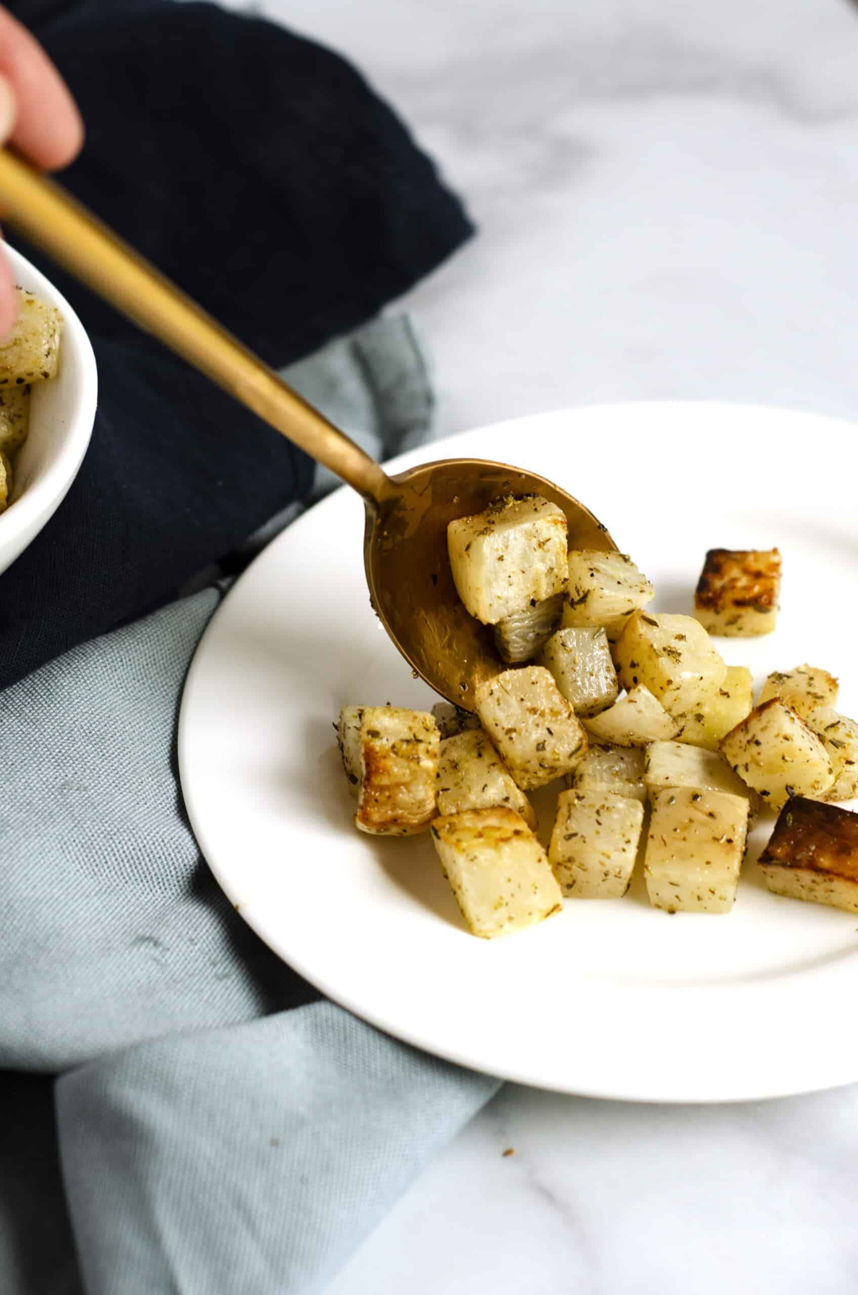 Gold spoon serving roasted turnips out onto a white plate