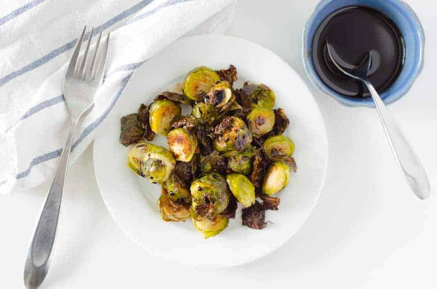 overhead view of a plate of brussel sprouts with a fork and a bowl of balsamic glaze