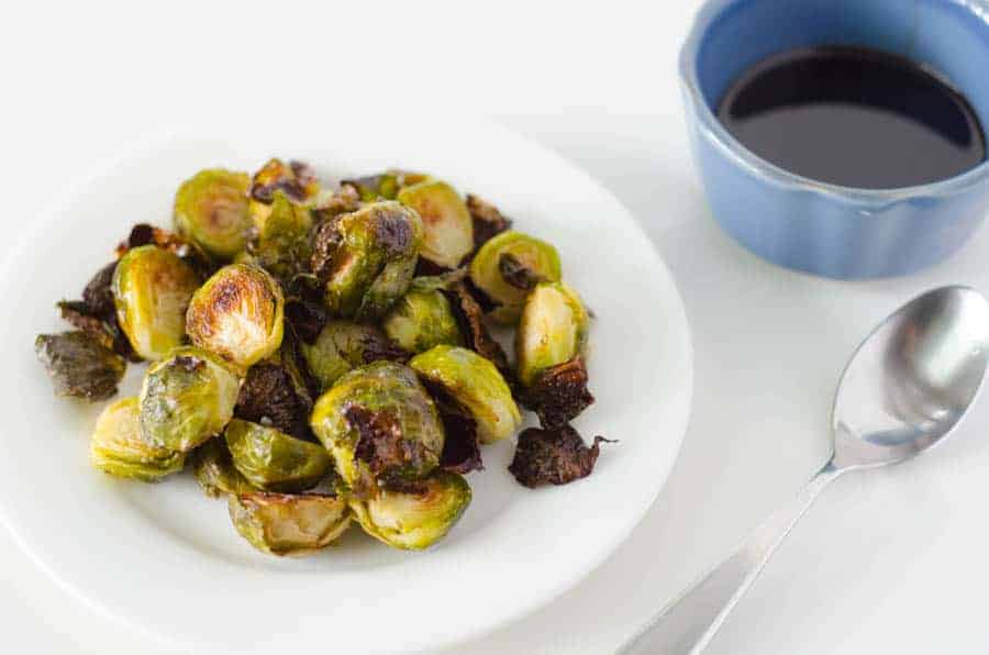 plate of roasted brussel sprouts with a spoon and bowl of balsamic glaze