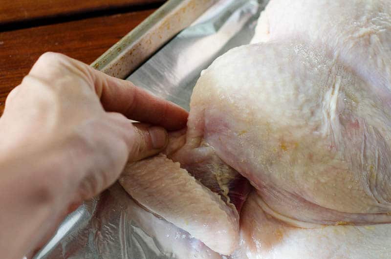 Person's hand tucking a chicken's wing under on a baking sheet