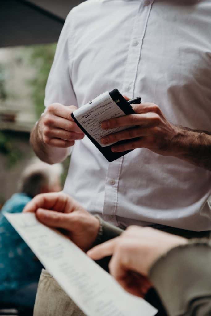 close up image of waiter's hand holding pad and diner's hand holding menu