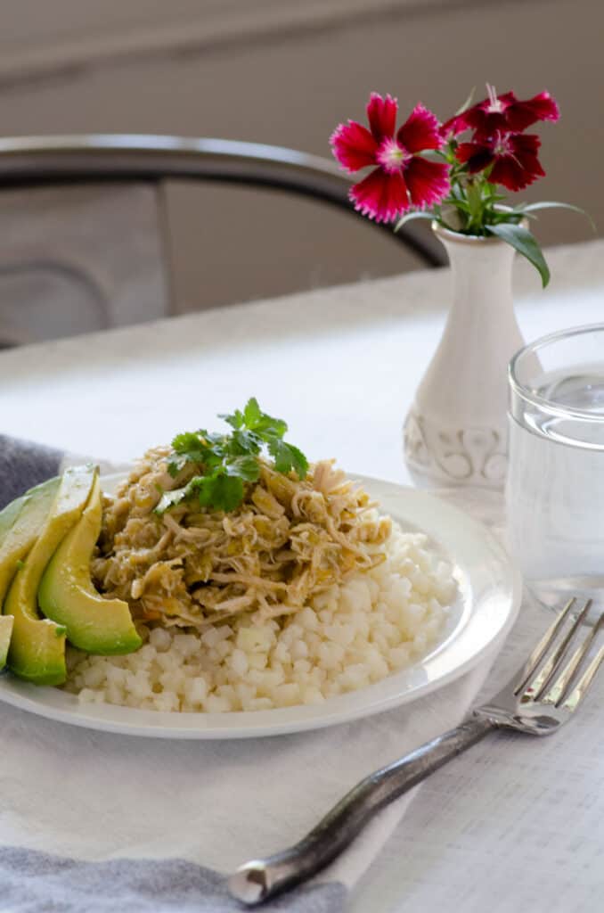 Green chile chicken plated on top of cauliflower rice topped with avocado and cilantro