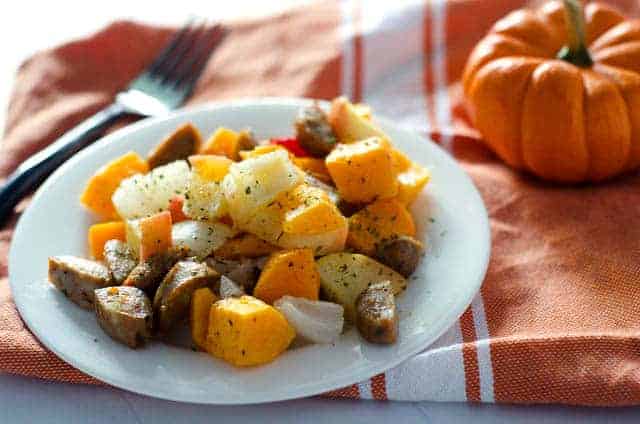 plate of sausage and vegetables on top of an orange napkin with a pumpkin in the background