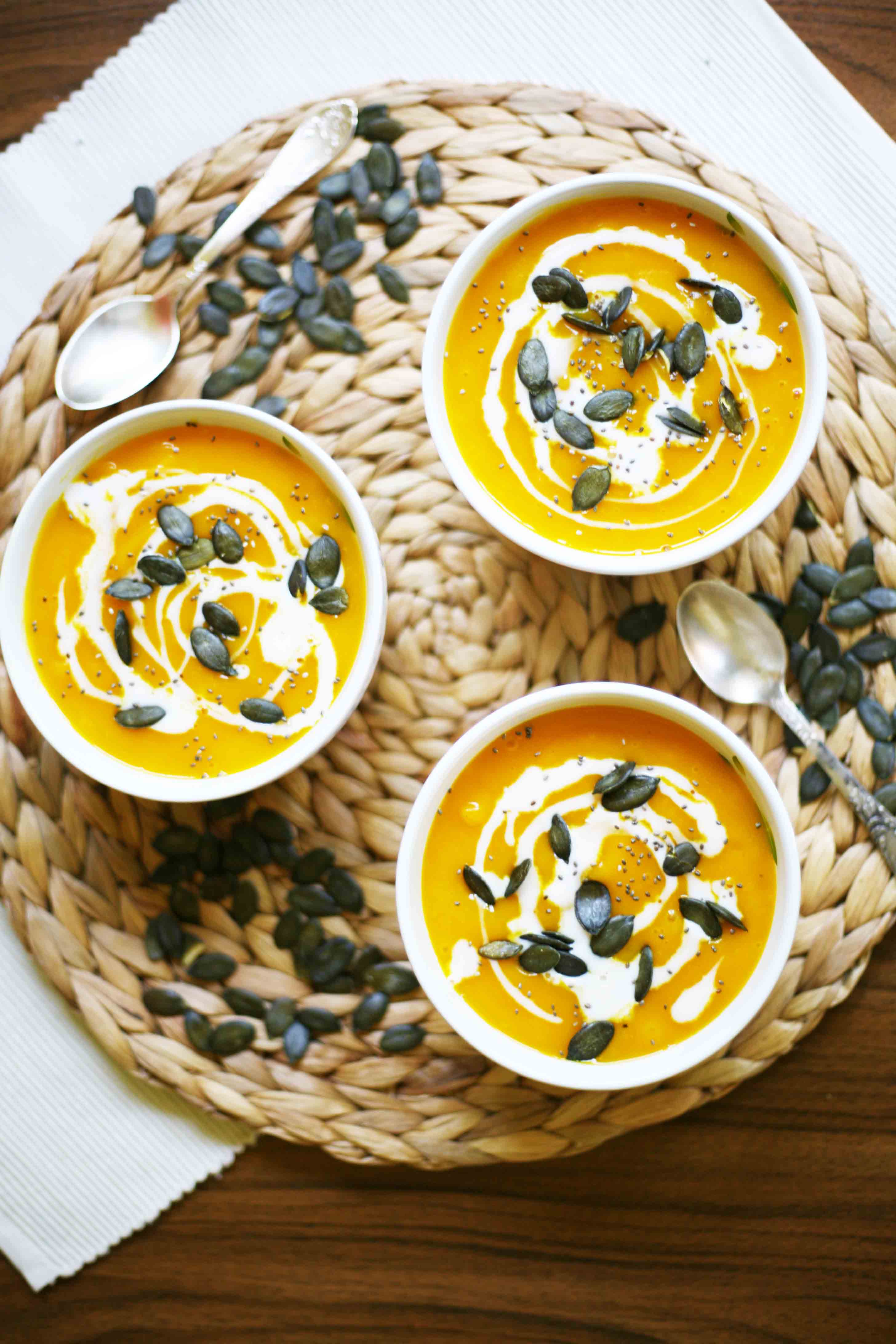 3 small white bowls from above with orange soup topped with pumpkin seeds and a swirl of white sauce