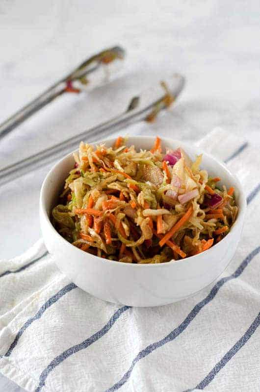 Vertical image of white bowl full of paleo coleslaw with tongs in the background