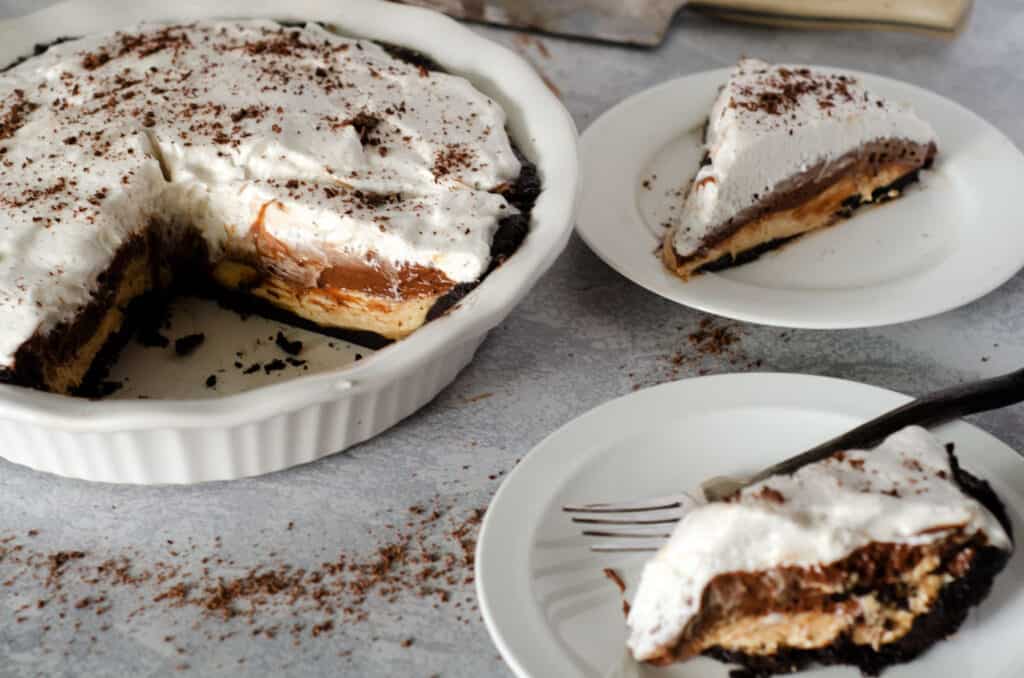 tabletop with chocolate peanut butter pie in pan with two slices on plates next to it and knife in the background