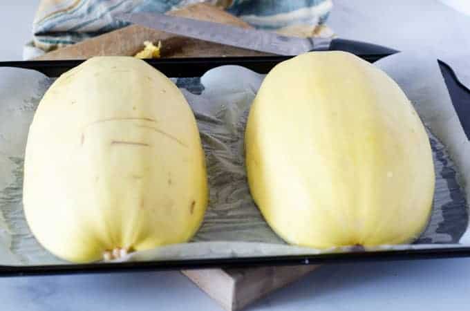 Two halves of spaghetti squash face down on a baking sheet