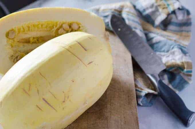 Spaghetti squash on cutting board cut in half with knife in the background