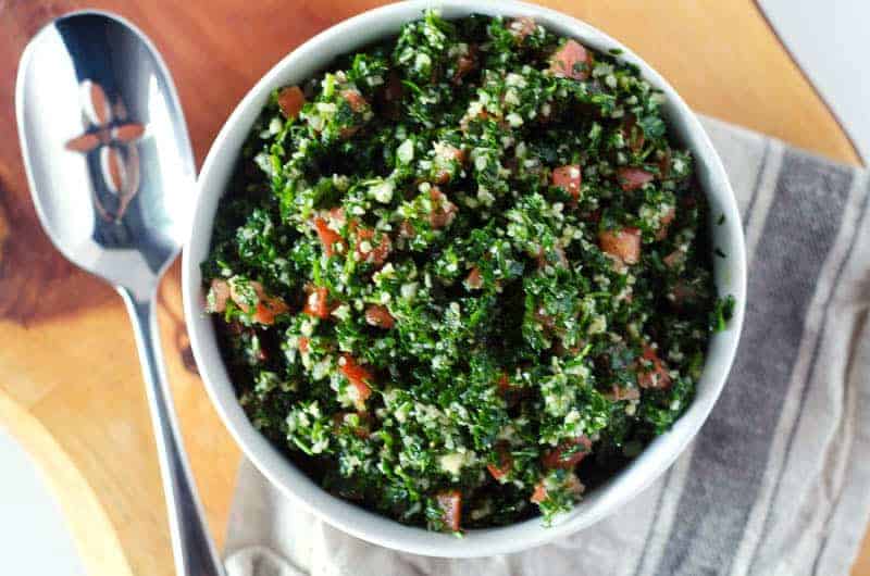 Overhead view of a bowl of cauliflower tabbouleh salad in a white bowl with a spoon and napkin